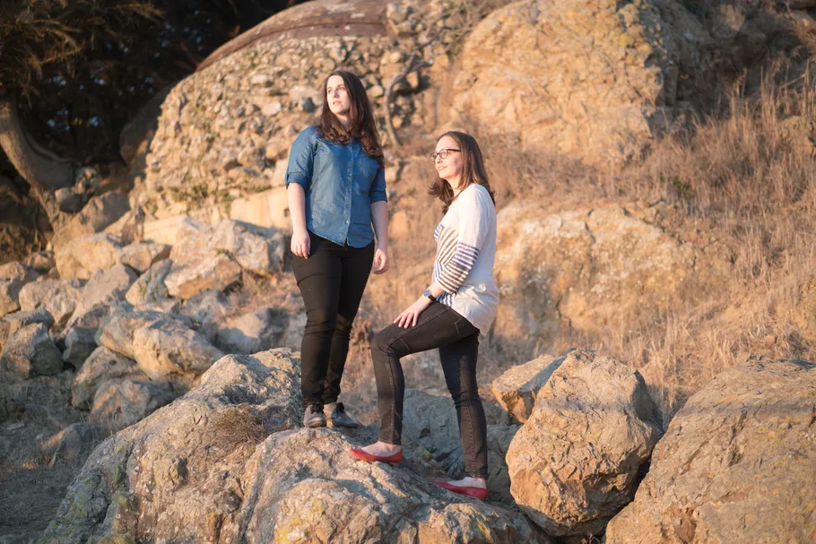 Emma and Julie standing on rocks by the beach, looking off to the side towards the sun